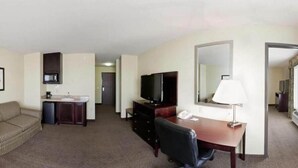 A hotel room with a kitchenette, a television, a desk with a chair, a large mirror, and a sofa. - Holiday Inn Express & Suites Eagle Pass by IHG (Eagle Pass)