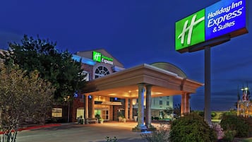 A Holiday Inn Express & Suites building with a prominent sign, a covered entrance, and a landscaped front area.
