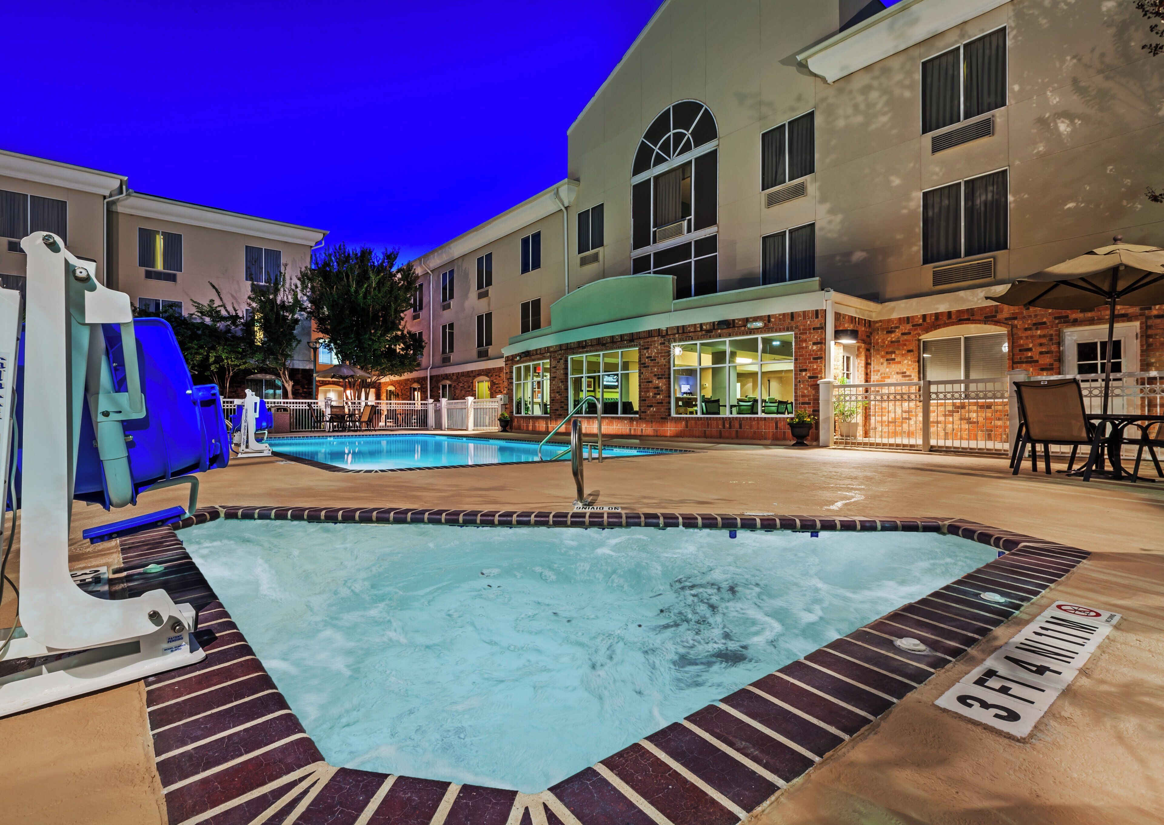 An outdoor swimming pool with a hot tub, surrounded by a brick building with a restaurant and outdoor seating.