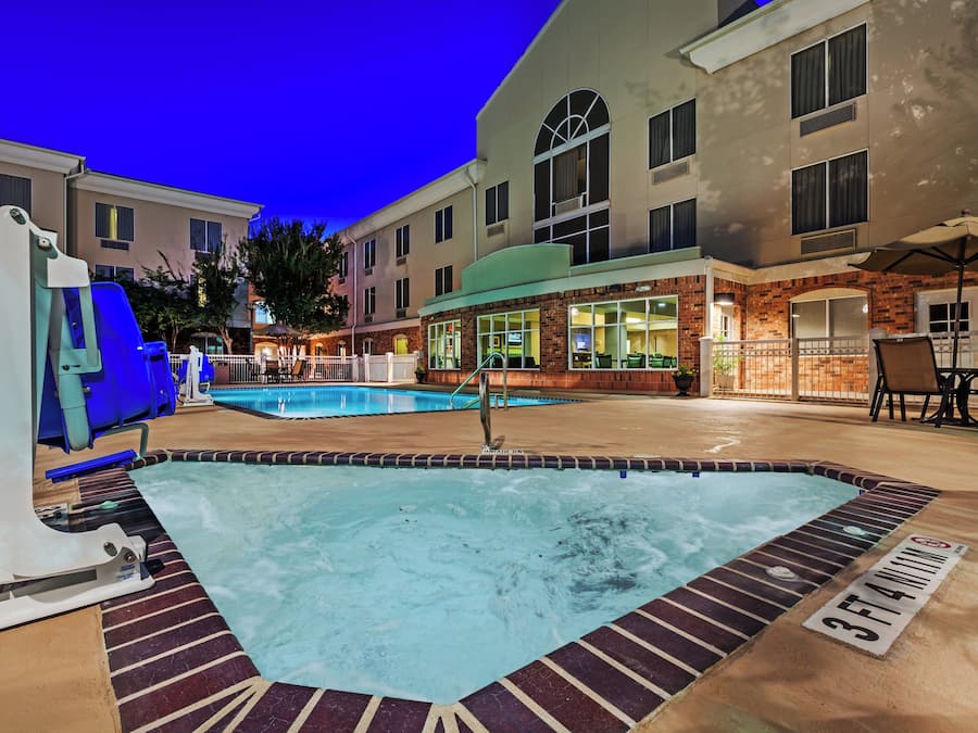 An outdoor swimming pool with a hot tub, surrounded by a brick building with a restaurant and outdoor seating.