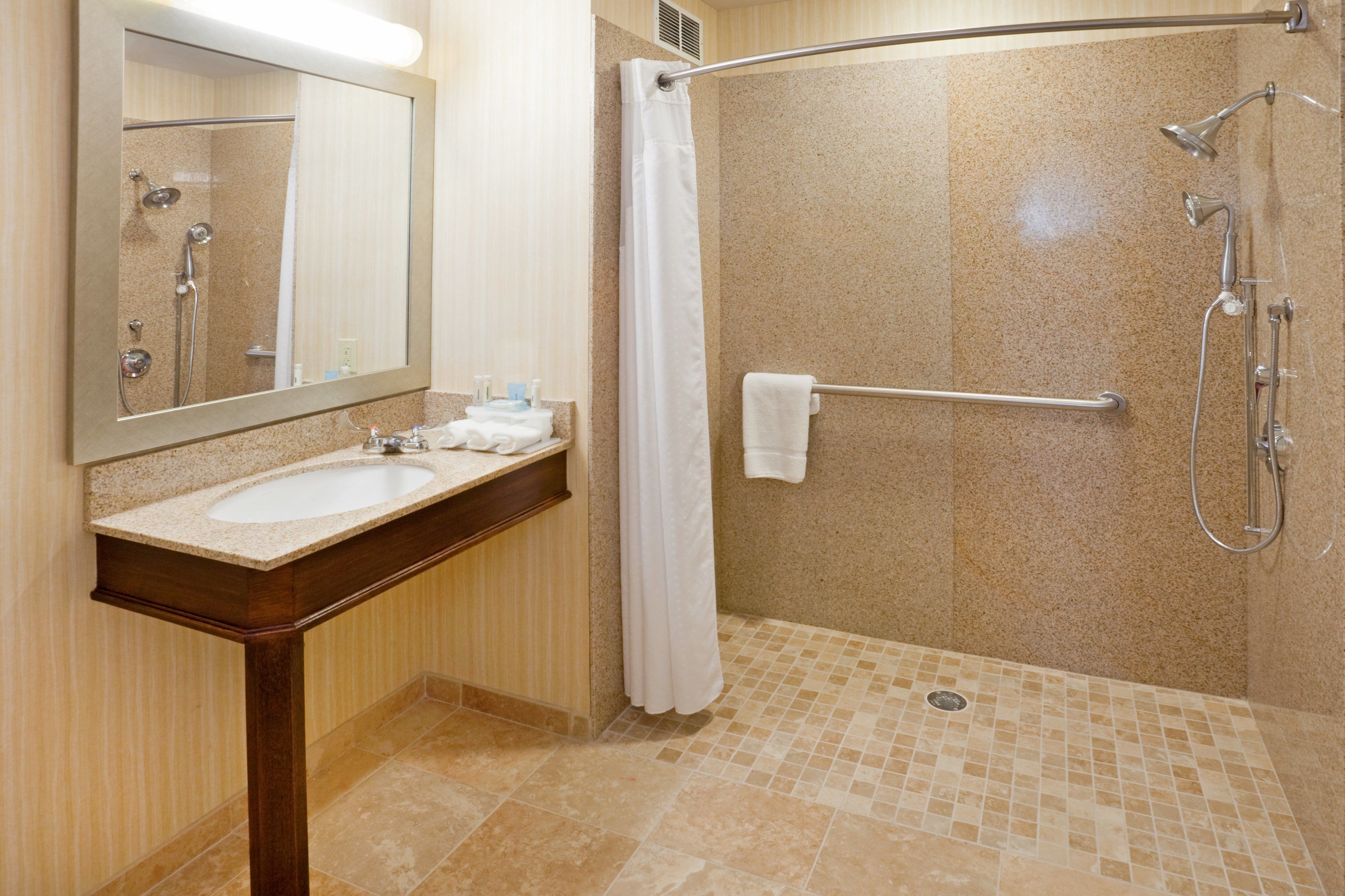 Un baño con lavabo, espejo, ducha y barra de apoyo.