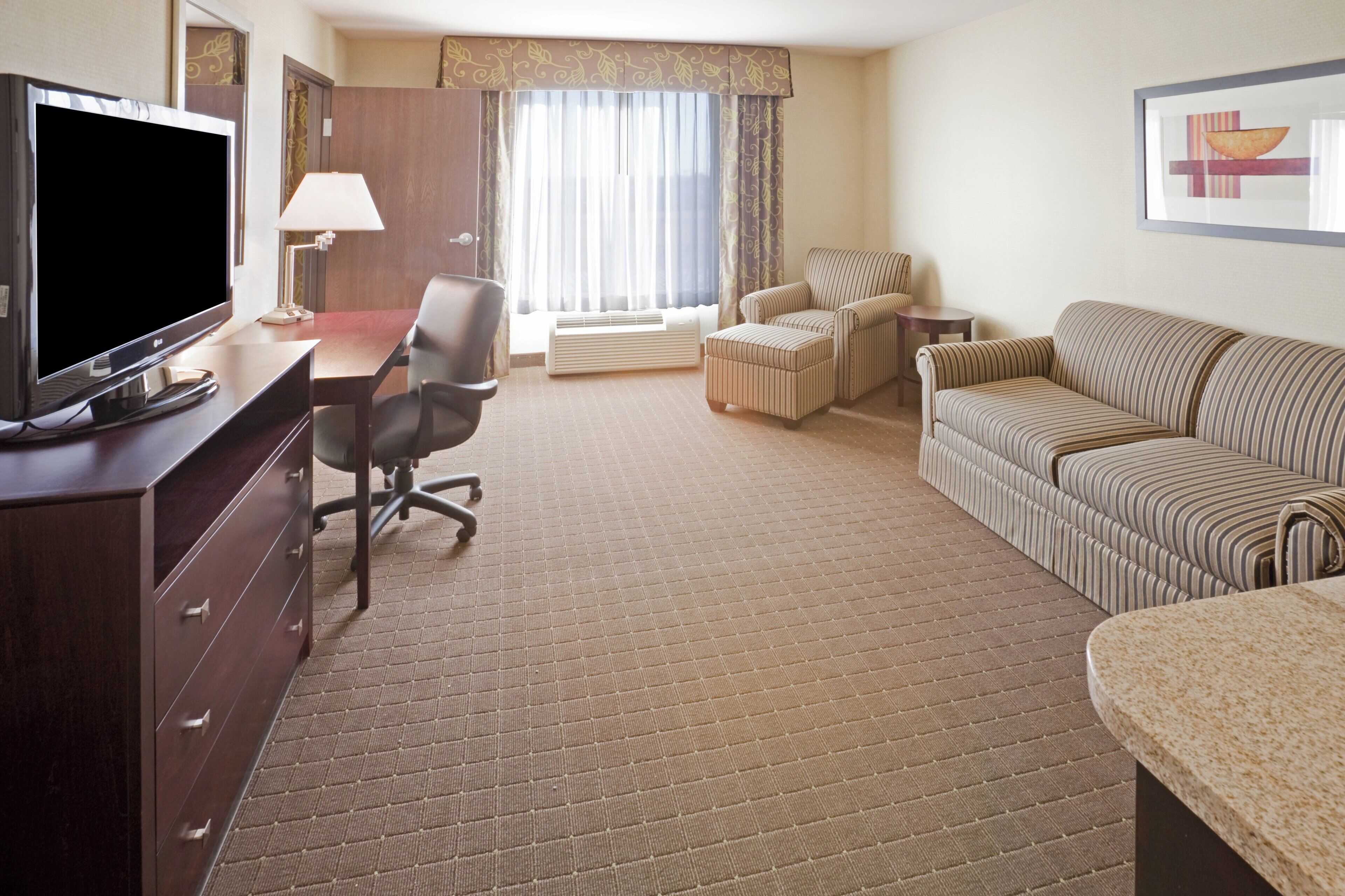 Ein Hotelzimmer mit Flachbildfernseher, Schreibtisch, Stuhl, Sofa und Bett.