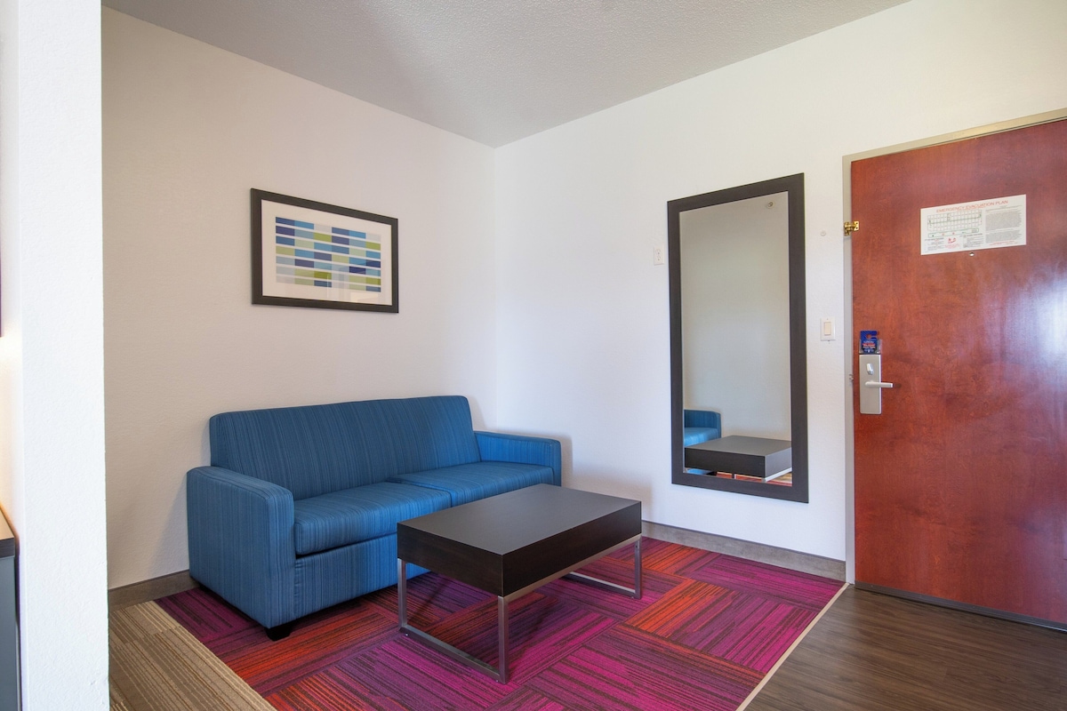 A room with a blue sofa, a small table, a mirror, and a door with an emergency evacuation plan.