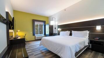 A hotel room with a bed, bedside tables, a desk, a chair, a TV, a window, and a wall-mounted lamp.