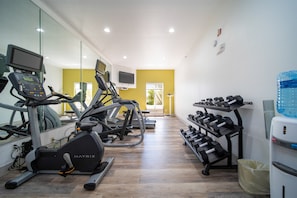 A gym with treadmills, a mirrored wall, a water dispenser, and a row of dumbbells. - Holiday Inn Express Hotel & Suites Bedford by IHG (Bedford)