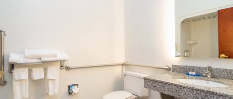 Un baño con inodoro blanco, lavamanos con encimera de granito y barandilla en la pared.