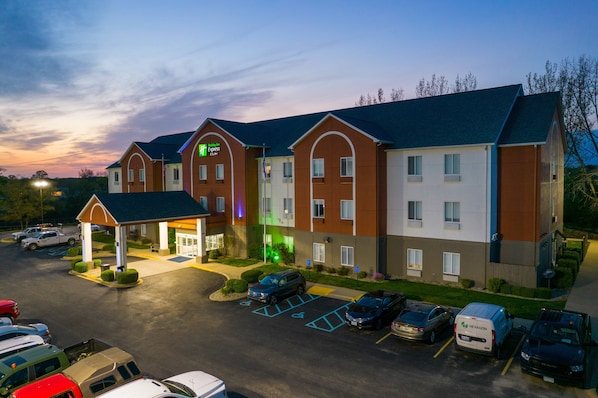 A multi-story hotel with a central entrance, parking lot, and a variety of vehicles parked in front. - Holiday Inn Express Hotel & Suites Bedford by IHG (Bedford)