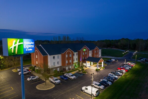 Un hôtel Holiday Inn Express & Suites doté d’un parking et d’un bâtiment dont l’entrée est illuminée de lumière verte.