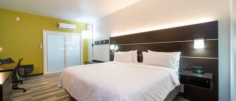 Une chambre d’hôtel moderne équipée d’un grand lit, de tables de chevet, d’un bureau avec une chaise et d’un appareil de climatisation.