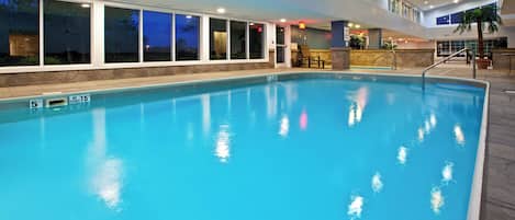 An indoor swimming pool with clear water, a diving board, and a stone wall surrounding it.