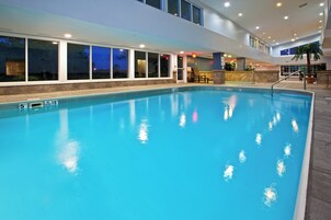 An indoor swimming pool with clear water, a diving board, and a stone wall surrounding it.