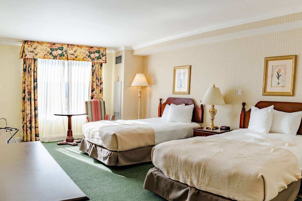 A hotel room with two beds, a desk, a chair, a lamp, and two framed pictures on the wall.