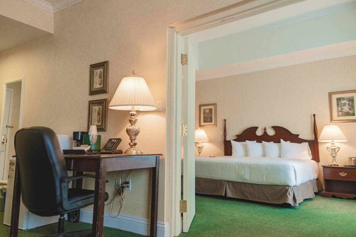 A hotel room with a bed, bedside tables, a desk with a lamp, and a chair.