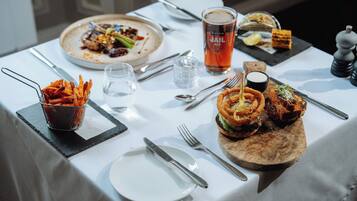 A dining table with a variety of dishes, including a burger with onion rings, a plate of fries, and a glass of beer.