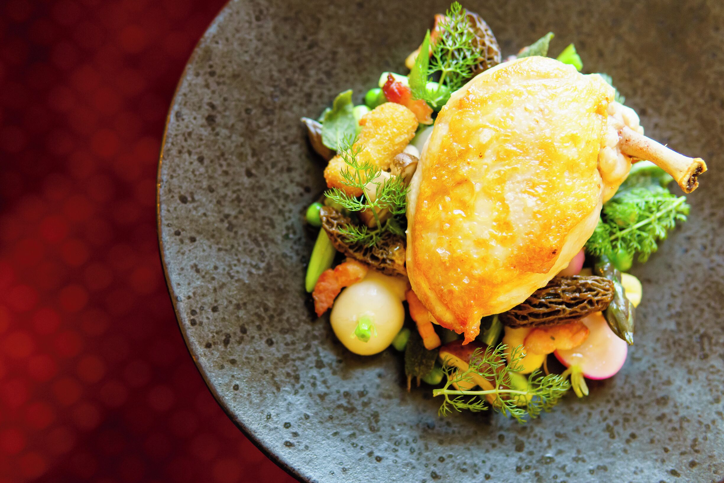 A dish with a golden-brown crust, garnished with herbs and vegetables on a textured plate.