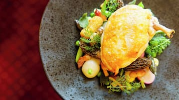 A dish with a golden-brown crust, garnished with herbs and vegetables on a textured plate.