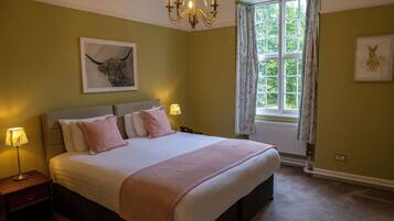 Um quarto com uma cama grande, duas mesas de cabeceira, um candelabro, uma janela com cortinas e obras de arte nas paredes.
