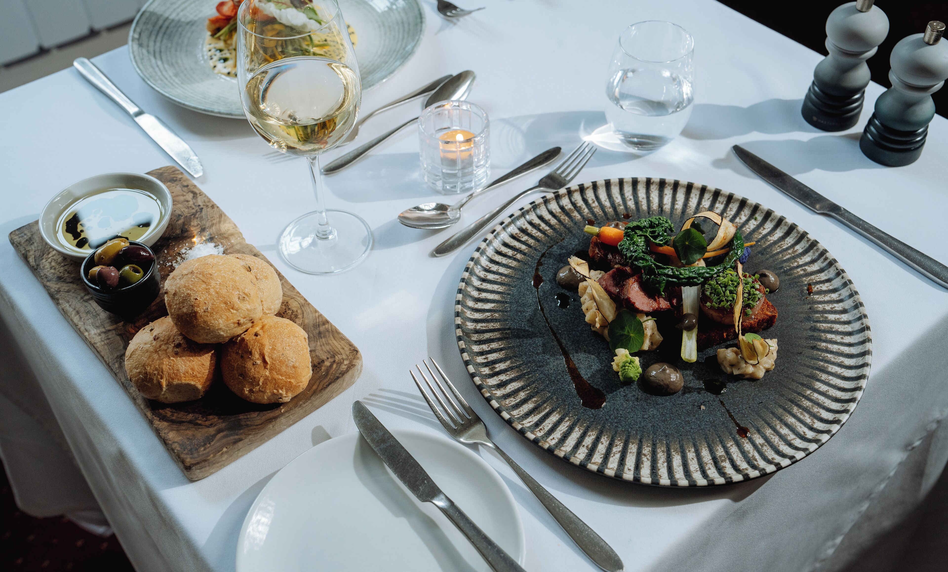 A table set for a meal with a plate of food, bread, and a glass of wine.