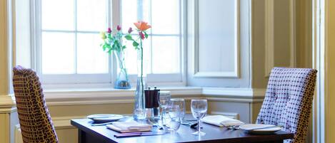 Una mesa de comedor dispuesta con cristalería, platos y un jarrón con flores.