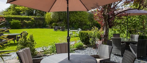 Un patio al aire libre con mobiliario de mimbre, una mesa redonda y una sombrilla grande que proporciona sombra.