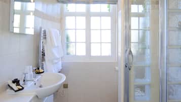 A bathroom with a white sink, a glass shower enclosure, and a window with a view of greenery.