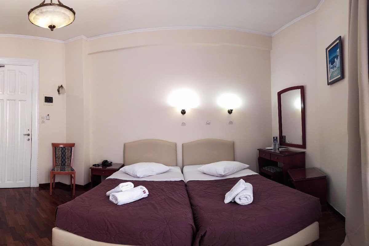 Habitación de hotel con dos camas, una silla de madera, una mesita de noche, un aparador y un espejo.