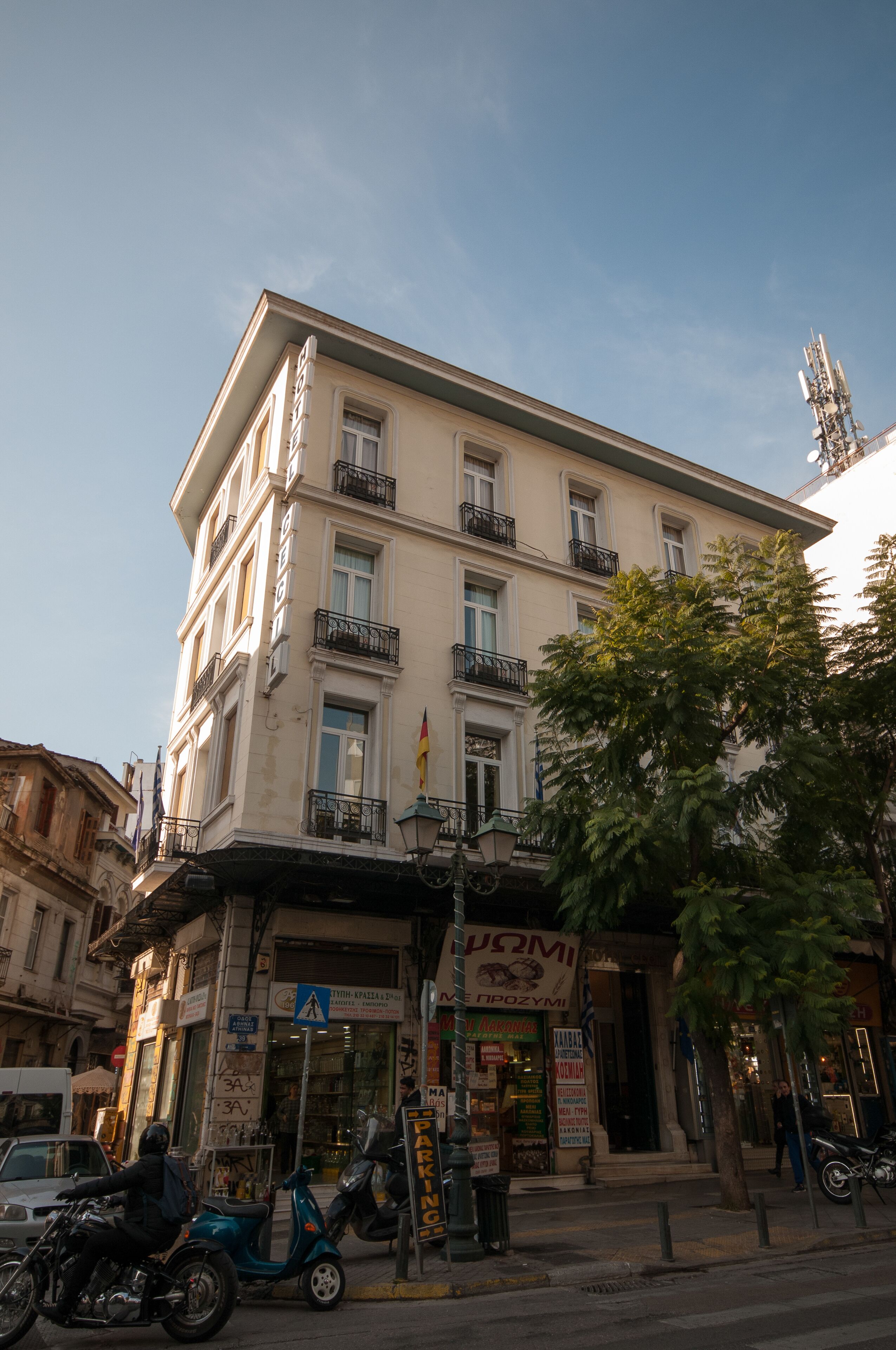 A multi-story building with a ground-floor shop, balconies, and a tree in front.