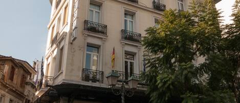 A multi-story building with a ground-floor shop, balconies, and a tree in front.