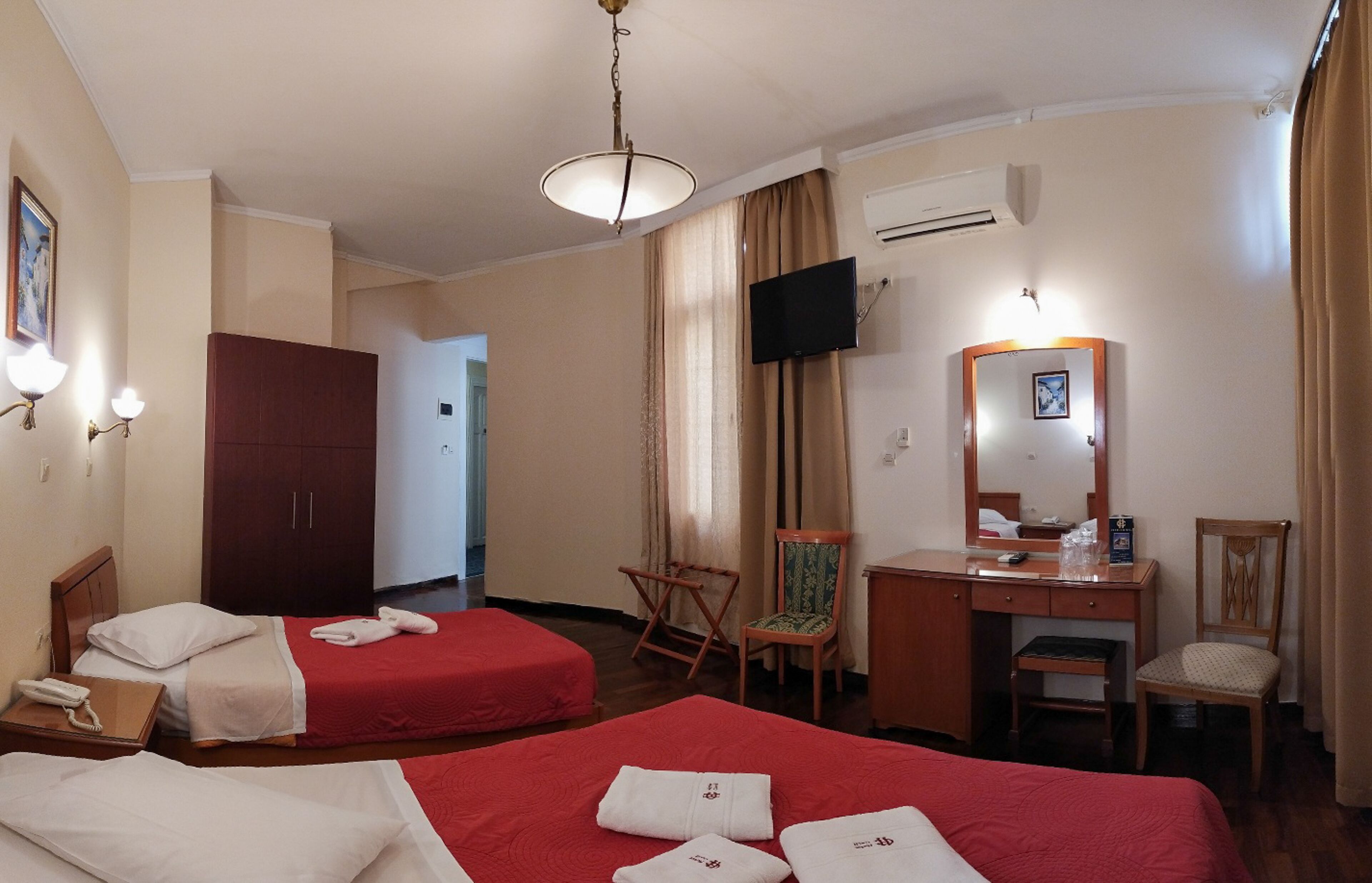 Ein Hotelzimmer mit zwei Betten, einem Schreibtisch, einem Sessel, einem Fernseher und einer Klimaanlage.