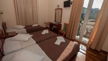 A hotel room with two beds, a desk, a chair, a TV, and a balcony with a view of buildings.