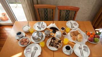 Una mesa de desayuno con huevos, tostadas, jugo, café y bollería.