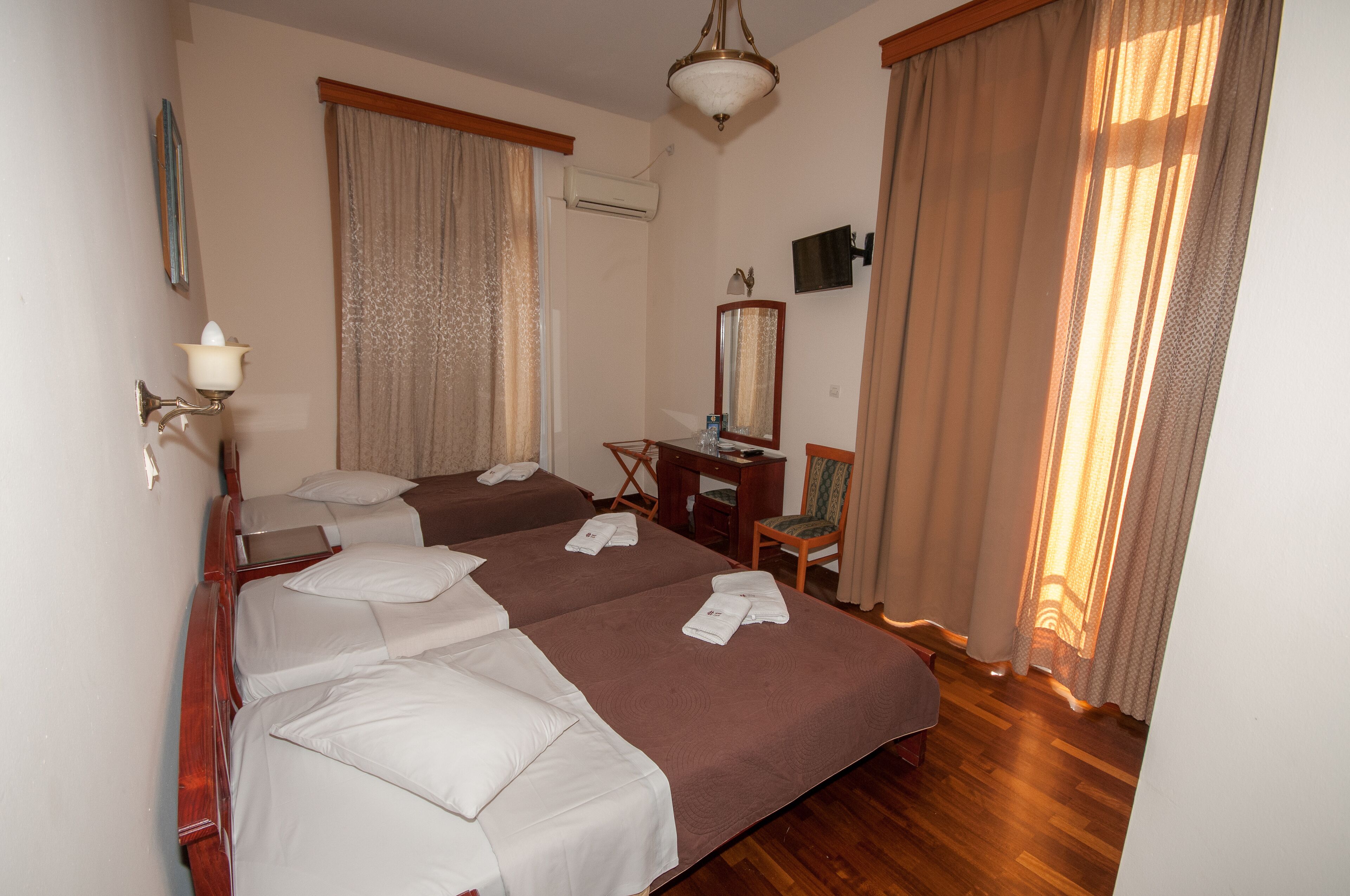Une chambre d’hôtel avec deux lits, un bureau, une chaise, un miroir et un téléviseur.