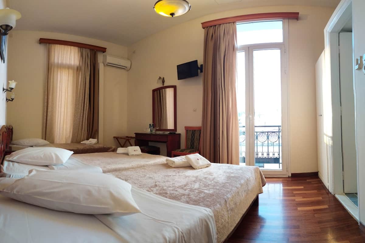Habitación de hotel con dos camas, un escritorio, una silla, un televisor y un balcón.