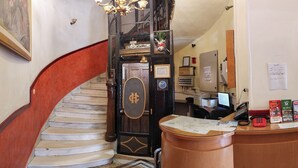 Un'elegante hall d'albergo con una scalinata in marmo, una reception e un lampadario, oltre a un quadro appeso al muro.