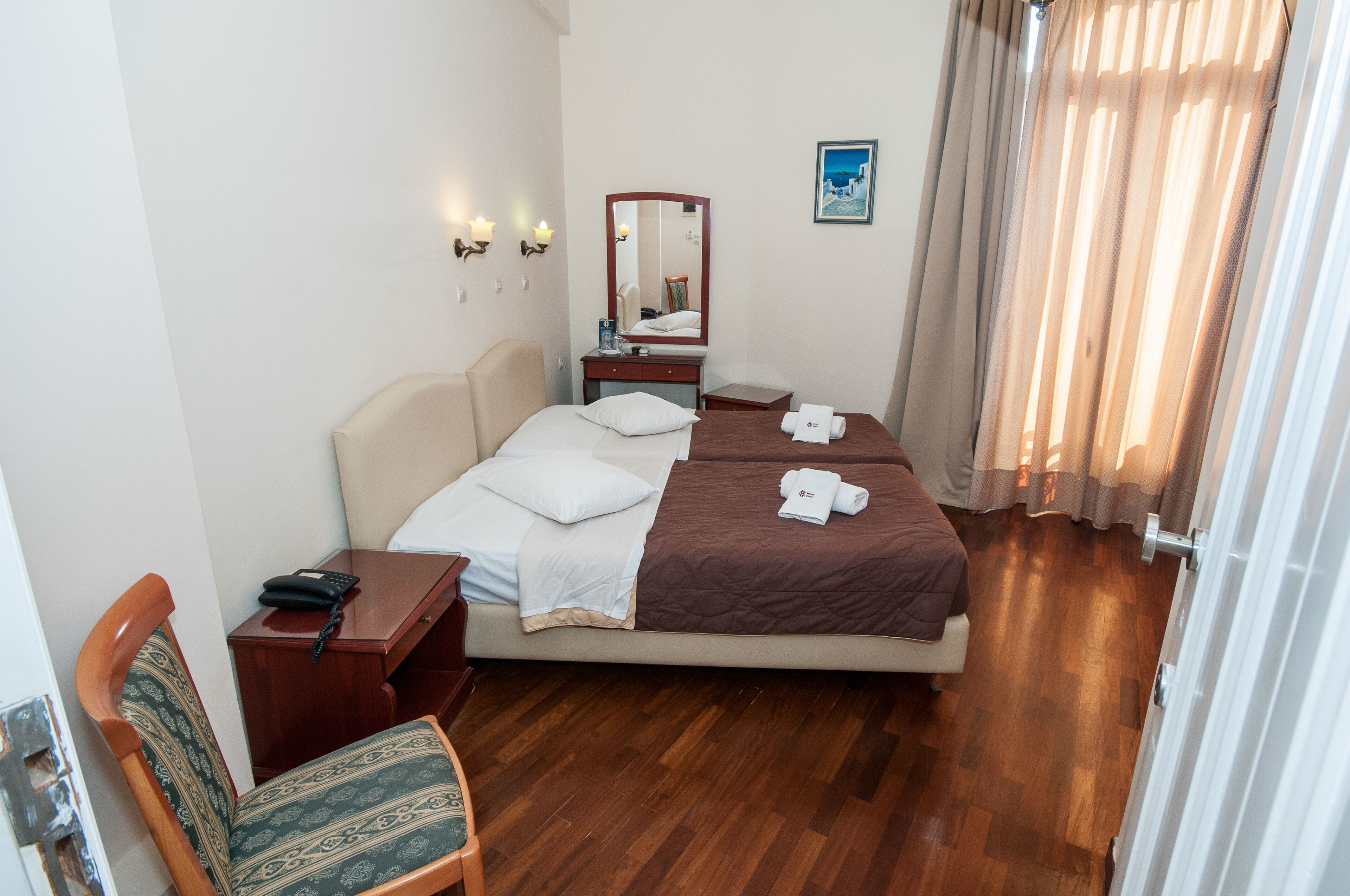 Une chambre d’hôtel comprenant un lit, des tables de chevet, un bureau, une chaise, un miroir et une fenêtre avec des rideaux.