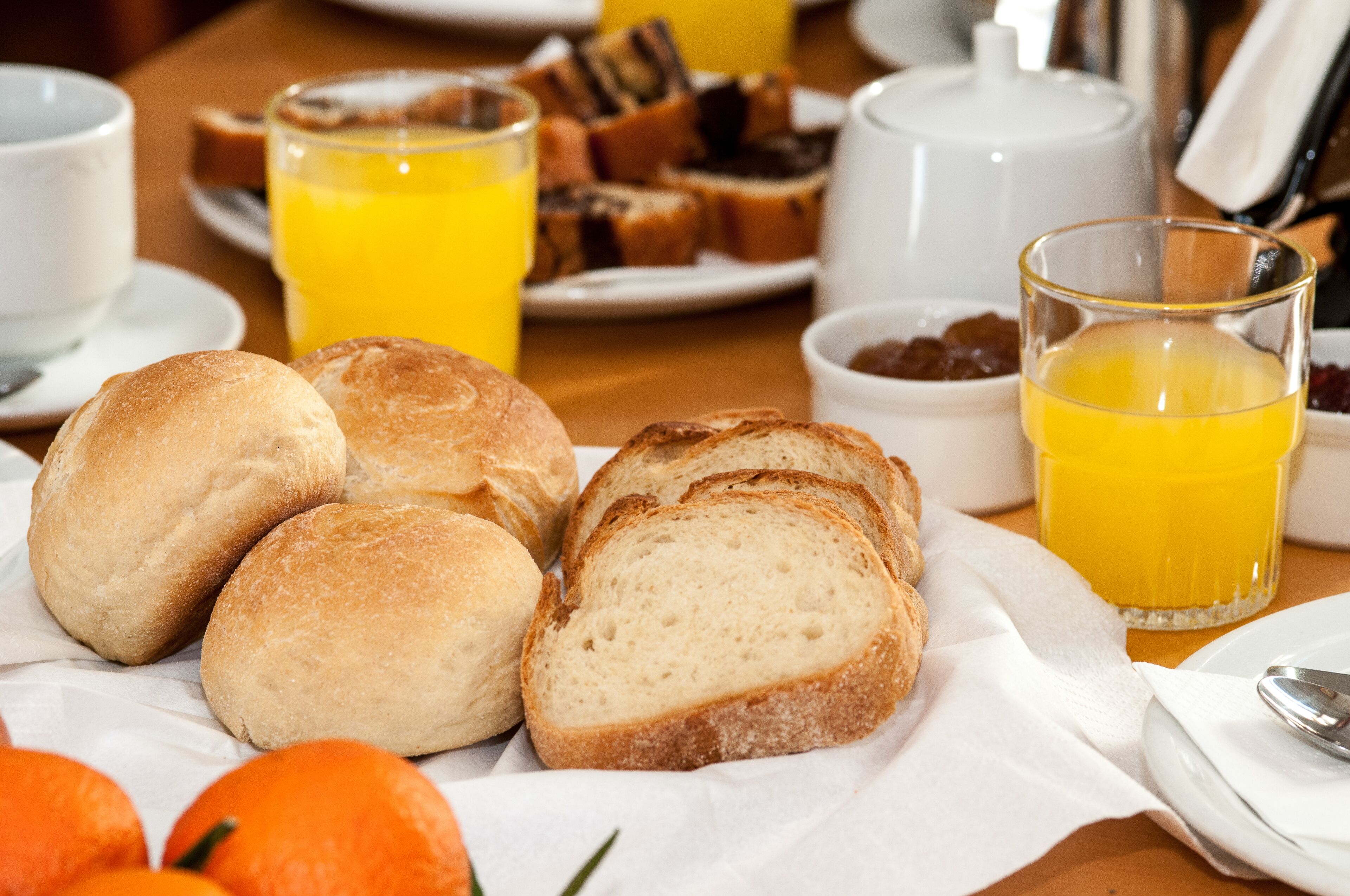 Ein Frühstückstisch mit Brot, Orangensaft und einem Teekännchen.