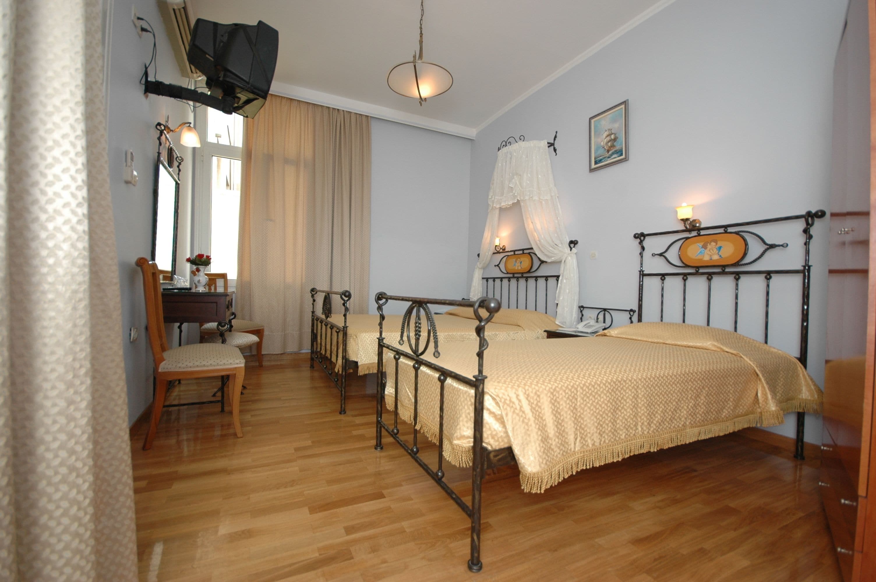 A bedroom with two single beds, wooden flooring, a desk with a chair, and a window with curtains.