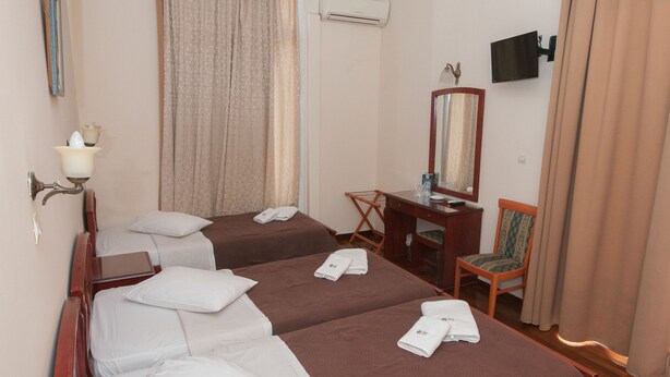 A hotel room with two beds, a desk, a chair, a TV, and an air conditioning unit. - Cecil Hotel (Athens)