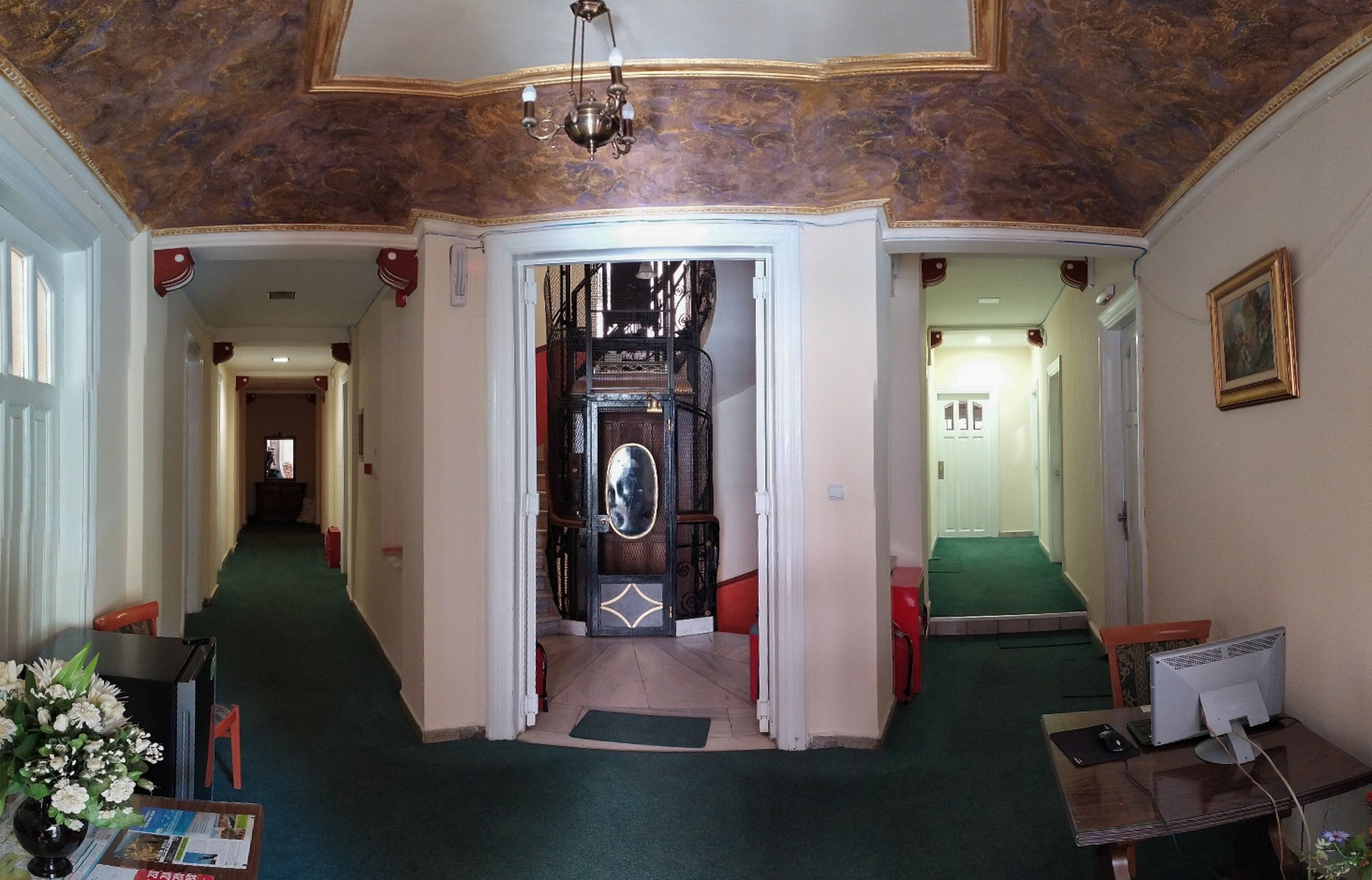 A hotel lobby with a grand staircase, a reception desk, and a computer setup.
