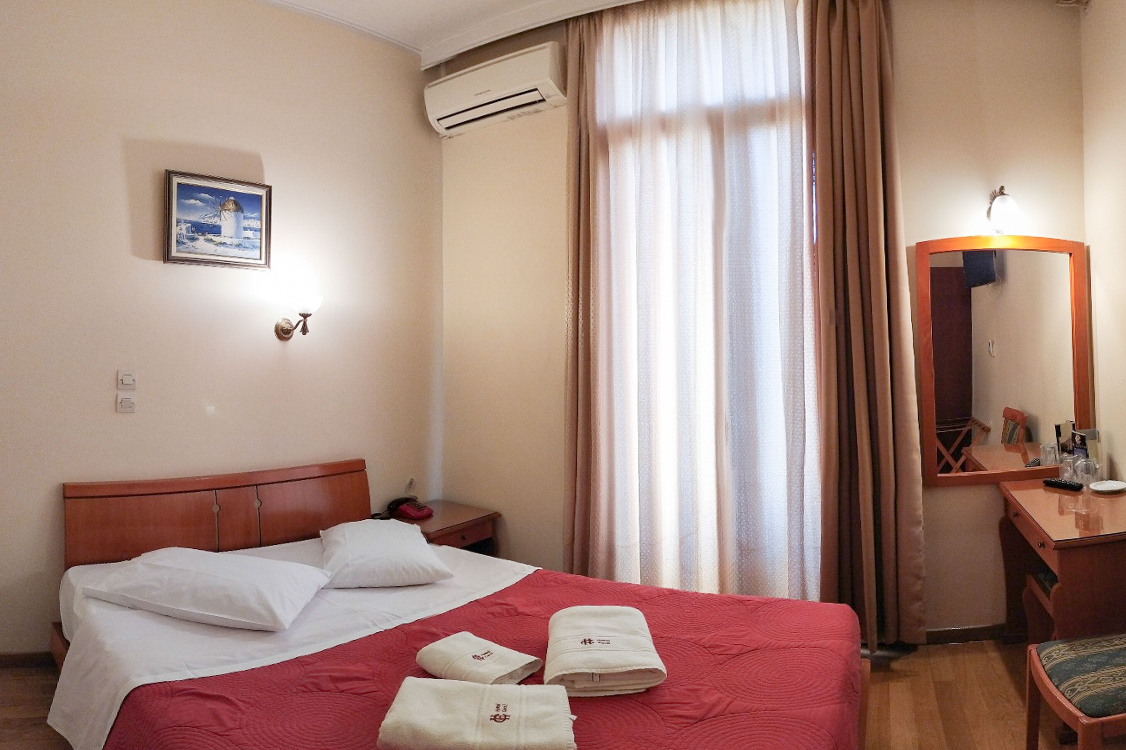 A hotel room with a bed, a desk, a mirror, and a window with curtains.