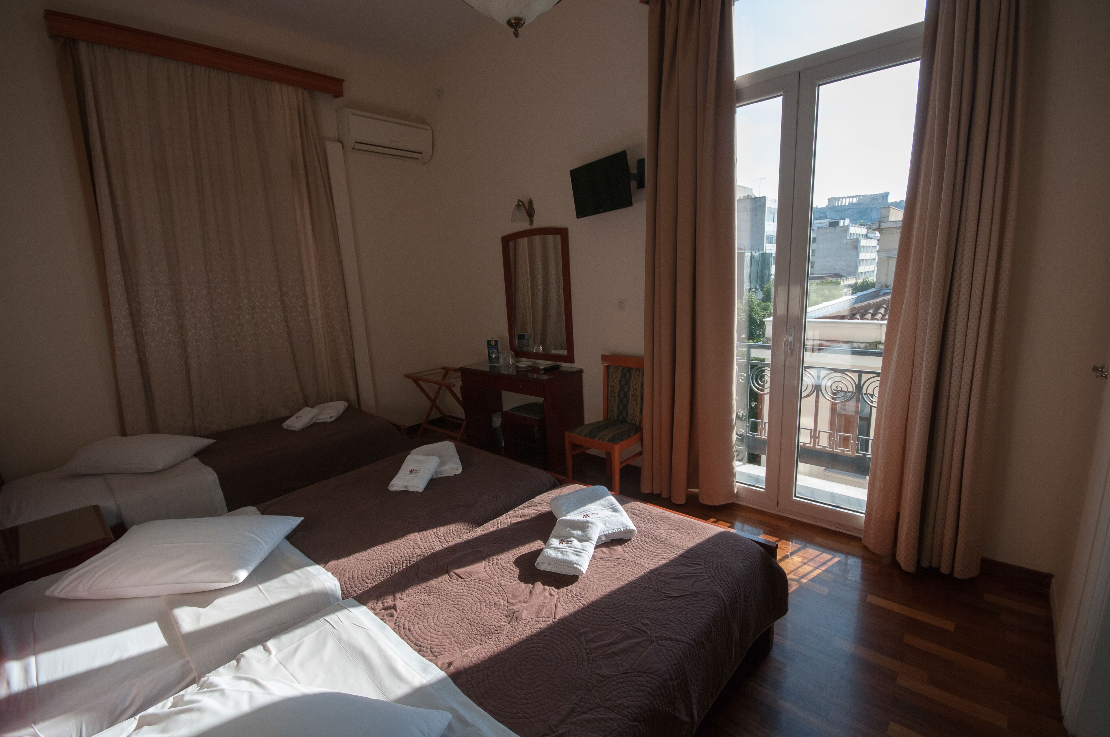 Habitación de hotel con dos camas, un escritorio, una silla y un balcón con vistas a edificios.