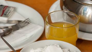 A dining table with a white bowl of whipped cream, a glass of orange juice, and a silver teapot.