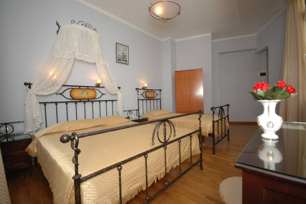 Un dormitorio con cama, mesitas de noche, aparador, armario de madera y un florero con flores.