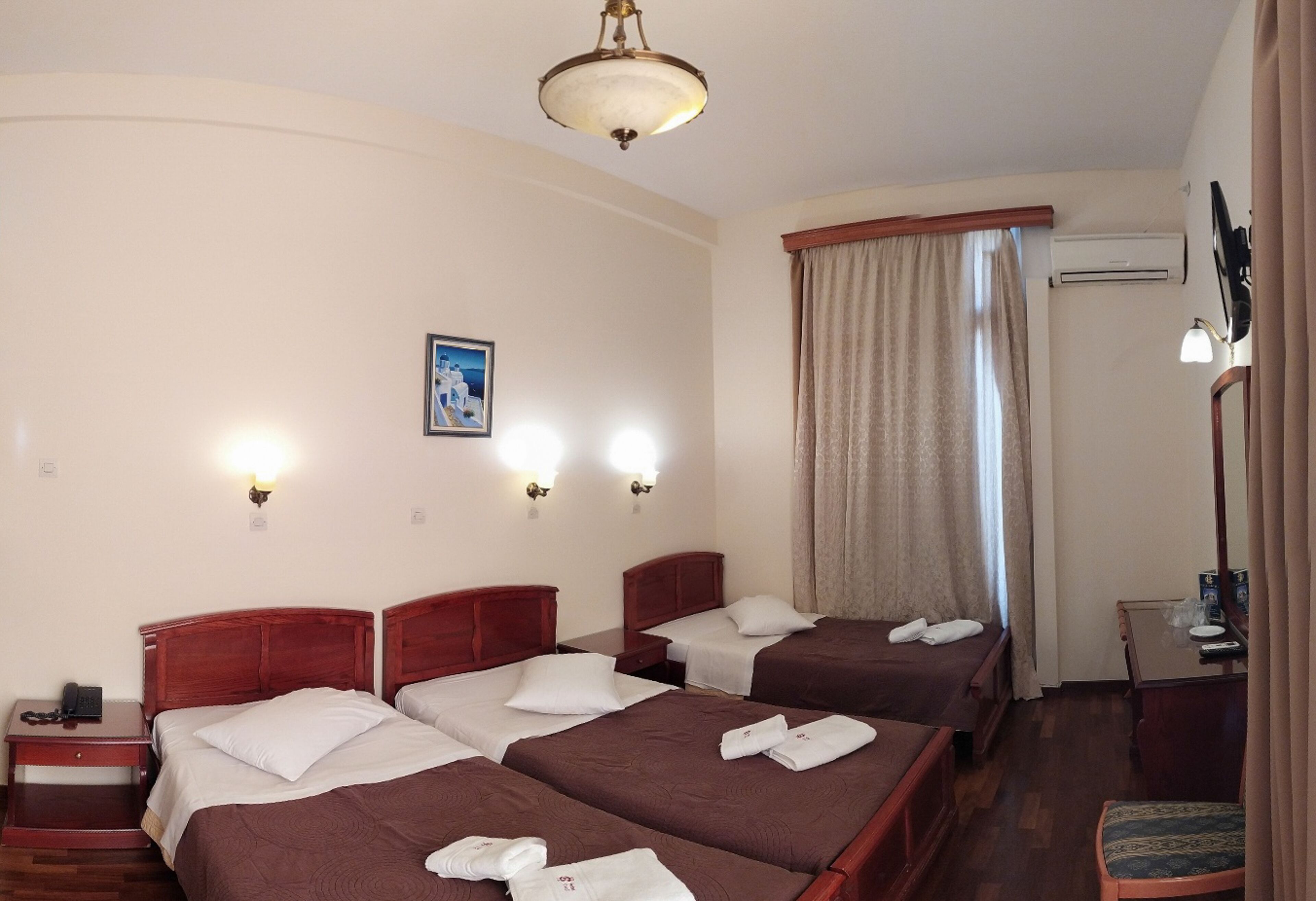 A hotel room with three beds, a desk, a chair, a telephone, and a picture on the wall.