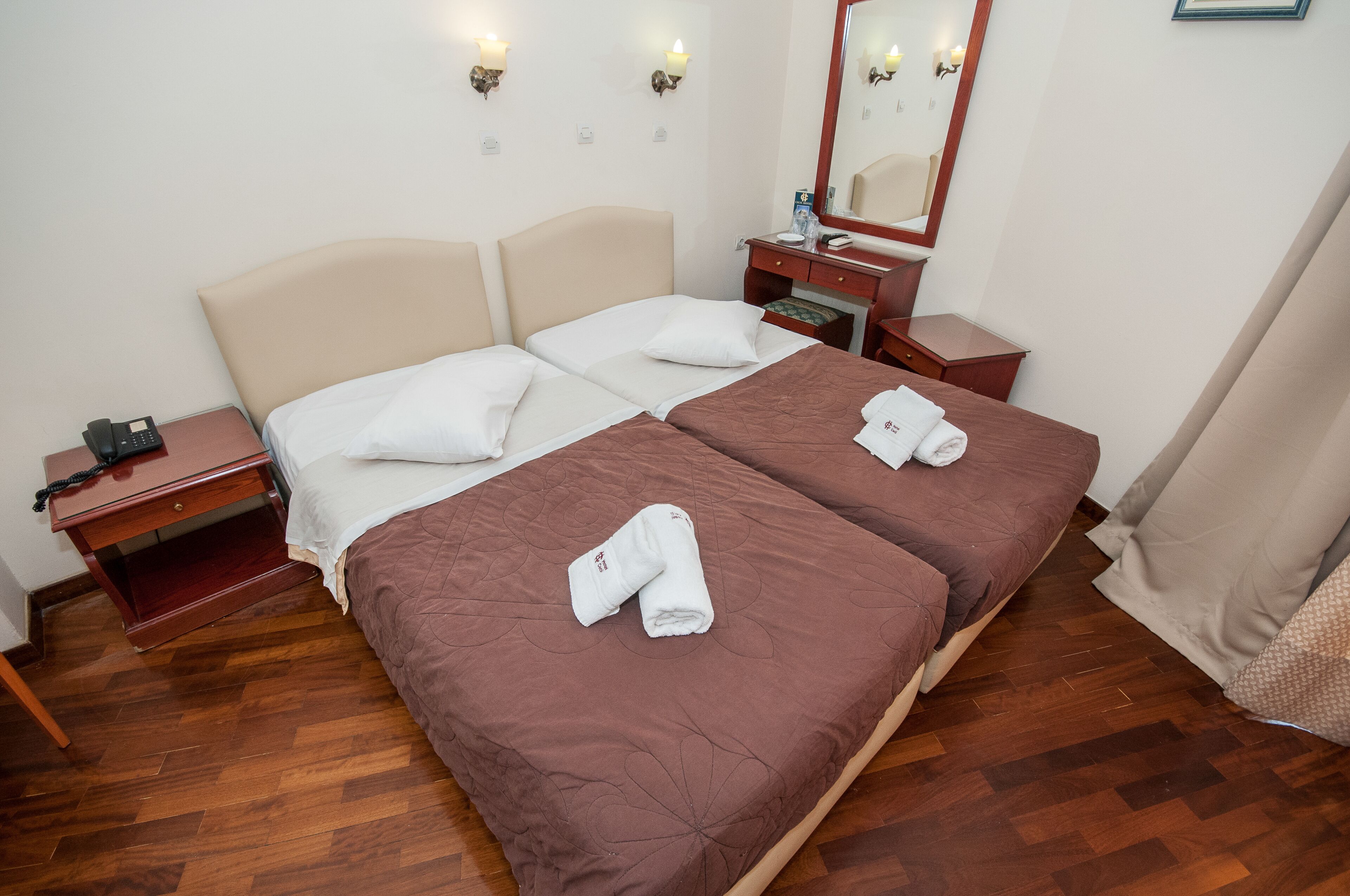 Ein Doppelbett mit zwei Kissen und einem gefalteten Handtuch auf jeder Seite. Ein Nachttisch aus Holz mit Telefon und Spiegel steht daneben.
