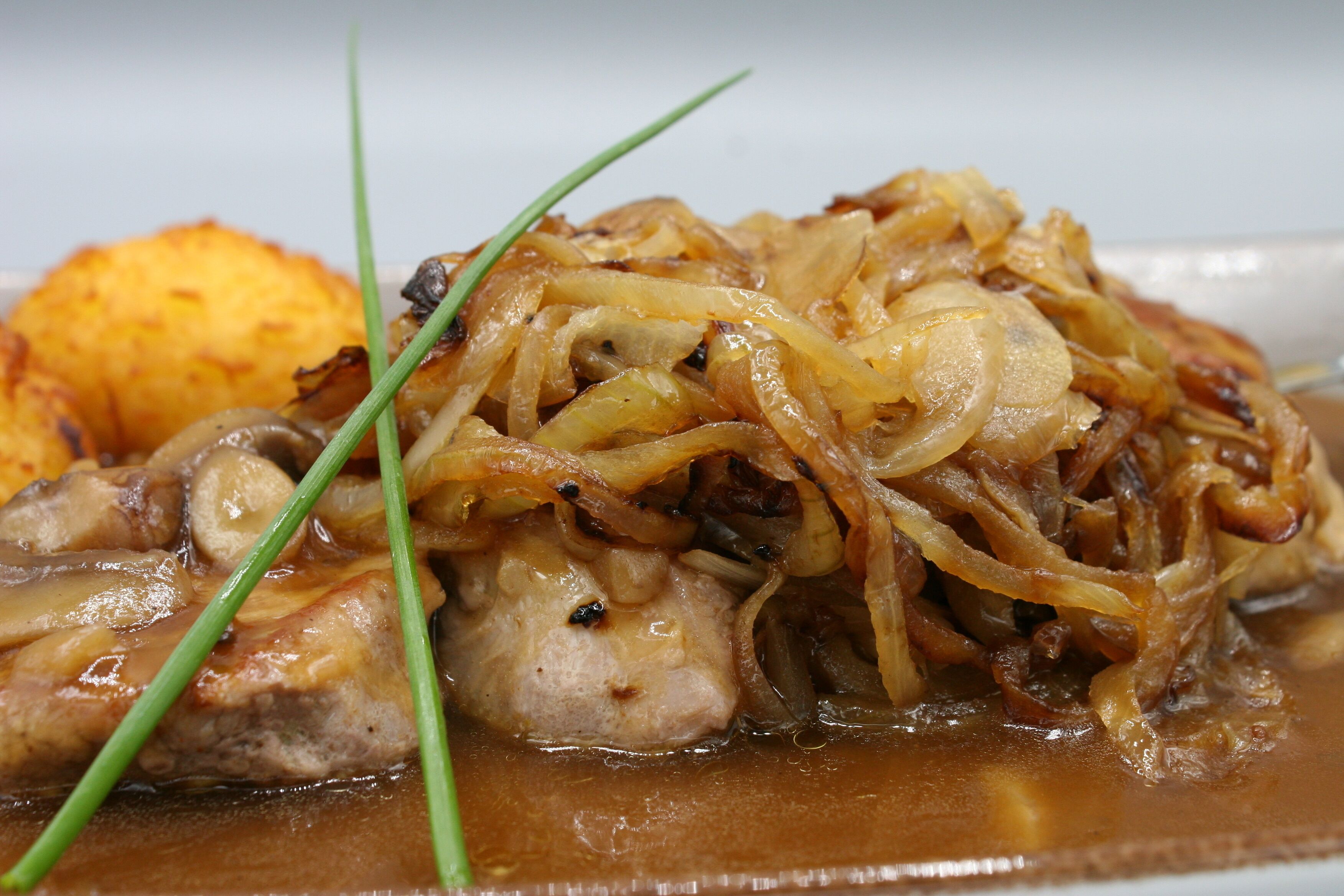 A dish with chicken, onions, and a side of potatoes.