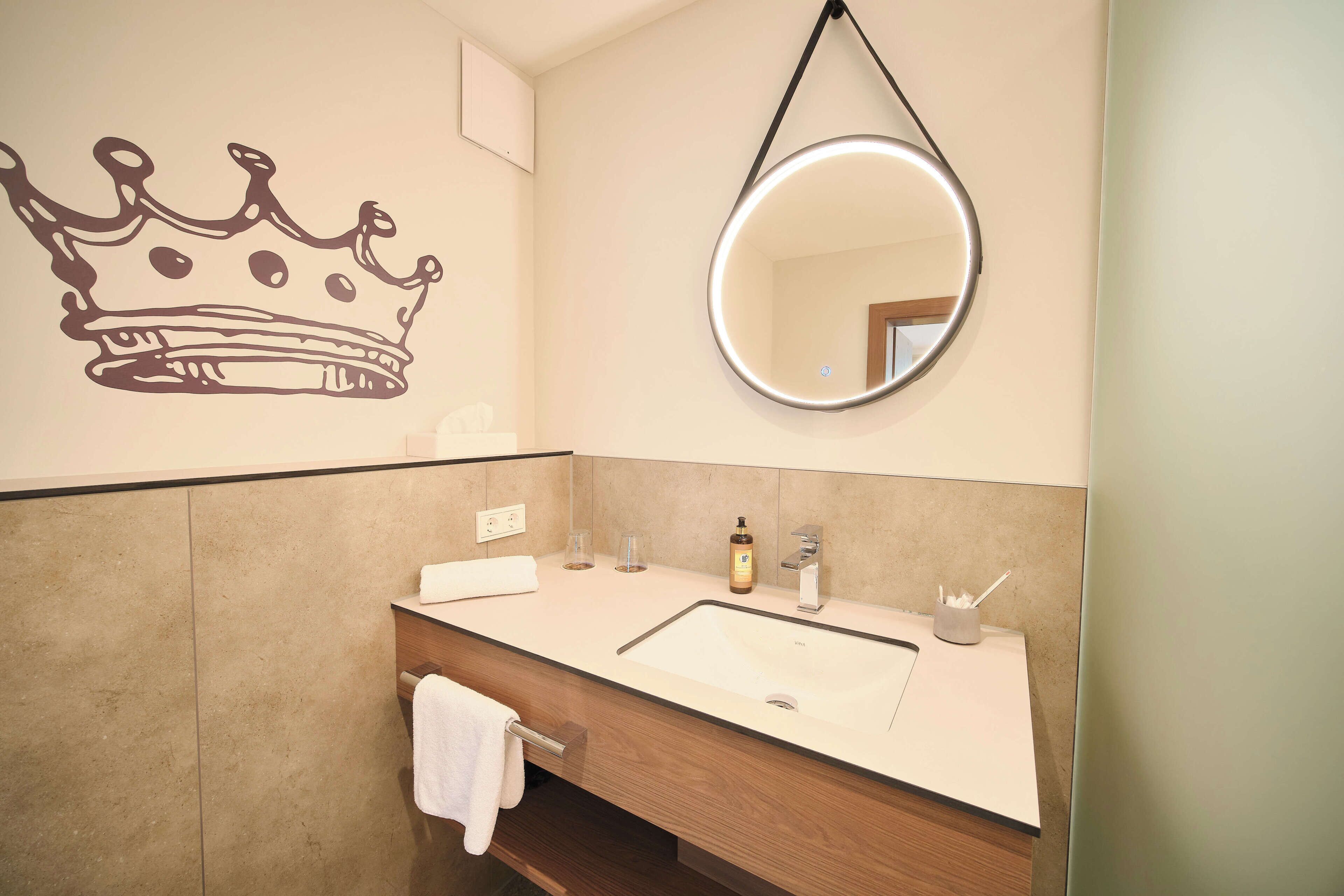 Ein Badezimmer mit Waschbecken, Spiegel, Handtuchhalter und einer Krone an der Wand.