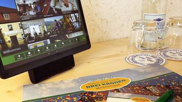 Un monitor de ordenador muestra un sitio web de hotel con varias secciones como 'Restaurante' y 'Servicio a la habitación'. También hay folletos y un bolígrafo sobre la mesa.
