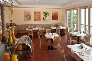 A dining area with multiple tables and chairs, a buffet station, and large windows offering a view of the outdoors. - Hotel & Brauereigasthof Drei Kronen (Memmelsdorf)
