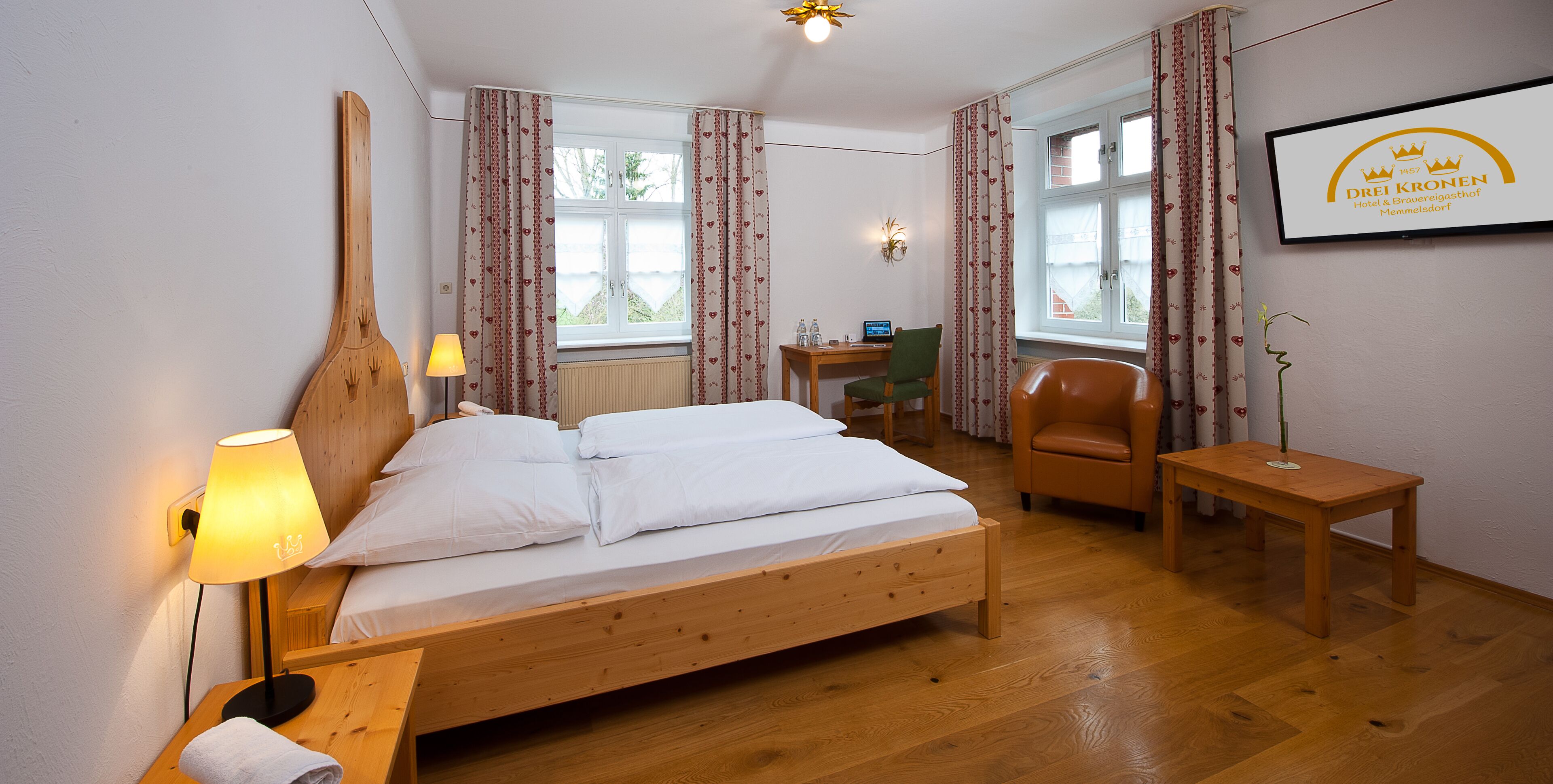 A hotel room with a wooden bed, a desk with a computer, a chair, and a small table.